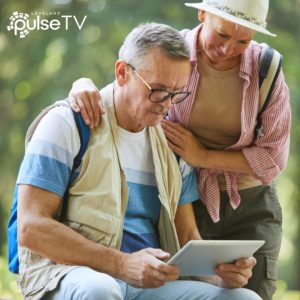 Photo of couple outdoors looking at a tablet. PulseTV log in the top left corner.
